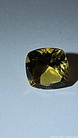 Photo of a cushion cut natural citrine gemstone with bright yellow color and high clarity on a light background.