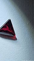 Close-up photo of the triangular fancy cut deep purple red heated natural sapphire gemstone showing polish and facet reflections.