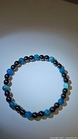 Top view of natural ocean blue agate and hematite bead stretchy bracelet laid flat in a circular shape on white background.