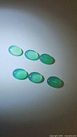 Six oval-shaped natural green onyx cabochon gemstones arranged in two rows on a white background under light illumination.