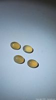 Four natural honey chalcedony oval cabochon gemstones displayed on a white background showing smooth, polished surfaces and honey-yellow color.