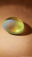 Oval cabochon lemon citrine stone lying on a brown surface with light reflection showing translucency and slight color variation.