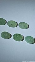 Photo of six natural mint green oval kyanite cabochons placed on white background showing color and internal inclusions.