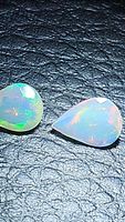 Close-up image of two faceted teardrop-shaped Ethiopian opals showing color flashes of green, blue, and orange against a black background.