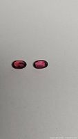 Pair of deep oval cut Padparadscha sapphires with orange, pink and red hues on a plain background.