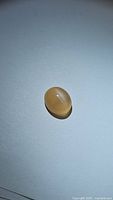 Image showing oval cabochon peach moonstone with visible catseye effect from top-down view.