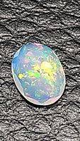 Close-up image of oval cut Ethiopian opal showing multicolored flashes on black background
