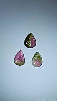 Three natural watermelon tourmaline gemstones with leaf cuts shown on a white background, displaying pink and green color zoning.