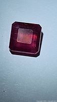 Close-up photo of square cut natural ruby showing red-pink hue and clarity characteristics under light.
