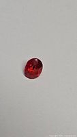 Oval cut natural sapphire gemstone with reddish-orange and blue colors on white background, photo from above.