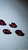 Four natural faceted red to pink sapphires arranged on a flat surface, various facets and shapes visible.