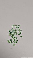 Photo showing multiple small round bright green tsavorite garnet gemstones scattered on a light background, highlighting their brilliant cut and uniform color.