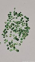 Multiple small round green Tsavorite garnet stones scattered on a neutral background, showing faceted cuts and vibrant green color.
