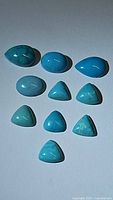 Top view of 10 polished turquoise cabochons in assorted shapes arranged on a white background, showing their vibrant robin's egg blue color and natural veining.