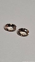 Clear, detailed photo of two oval cut natural untreated champagne morganite gemstones placed on a plain light background showing facets and color.