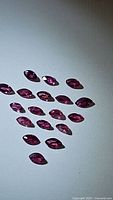 Photo of 18 natural untreated marquis cut rubies with bright deep pink to red color and high clarity displayed on white surface.