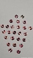 Loose round brilliant-cut padparadscha sapphires arranged on white background showing color variation and clarity.