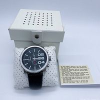Watch on cushion beside box and booklet