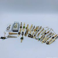 Full layout of all approximately 26 gold-tone tie clips showing variety of styles, enamel colours, chains and boxed pieces