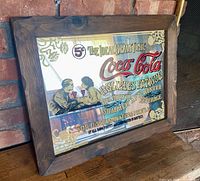 Full view of framed Coca-Cola mirror on floor against brick wall