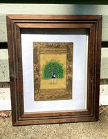 Full view of framed Indian miniature peacock painting leaning against wall