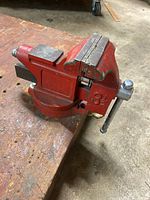 Side view of red bench vise showing jaws, body, base and handle