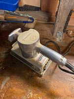 Angled view of palm sander with cord on workbench