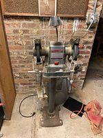 Front view of Sears Craftsman bench grinder on pedestal stand showing grinding wheels, lamp, spark guards, work rests