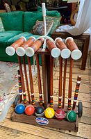 Full view of croquet set on wooden stand showing mallets, balls, stakes, and wheels
