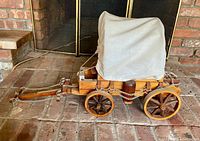Side view of miniature covered wagon showing wood body, wheels, canopy and chains