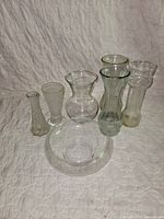 Group shot of all seven clear glass pieces: six vases and one bowl