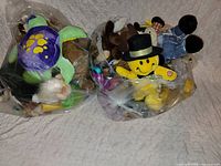 Two clear plastic bags filled with various plush toys including green-purple turtle and yellow smiley face plush
