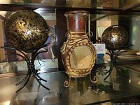 Two glass spheres on metal stands flanking ceramic lantern vase inside cabinet