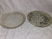 Two of the five clear pressed-glass trays; left with Christmas tree design, right with starburst/geometric design