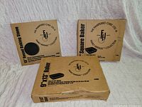 Three Pampered Chef boxes labelled 13" Round Baking Stone, 9" Square Baker, 9"x13" Baker