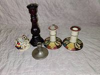 All five items grouped: tall glazed candlestick, two floral ceramic candlesticks, metal candleholder, small holiday figurine