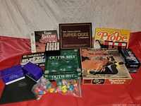 Photo of vintage board and card games including Triple Yahtzee, Super Quiz, Probe, Rummikub, Outburst, Dealer's Choice, Penny Arcade, and assorted game pieces in purple boxes and bags.