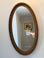 Full view of an oval mirror with a decorative gold frame hanging on a wall, showing its size and shape.