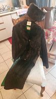 Photo of long dark brown fur coat draped over a chair with matching fur hat placed on top, showing full length and texture of the coat.