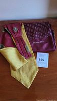 Two-tone burgundy and mustard yellow scarf with Christian Dior logo and medallion pattern, folded and displayed on wooden surface with auction tag