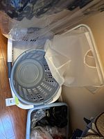 Three laundry baskets placed on wooden floor: one large rectangular white plastic basket, one small round white basket, and one foldable fabric basket with frame.