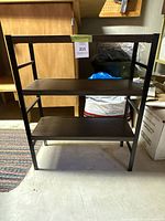 Front view of a metal shelving unit with three dark shelves on a black frame.