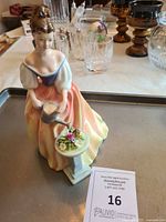 Front view showing woman in dress holding watering can next to pedestal with flowers