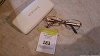 Eyeglasses laid out next to white Versace case and auction tag on surface