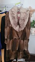 Full view of the women's Eaton's fur coat hanging on a rack, showing the full brown fur body with large light fur collar.