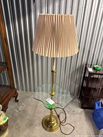 Full view of brass floor lamp with pleated shade and glass shelf