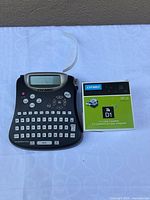 Label maker with tape cassette boxed, tape protruding from device