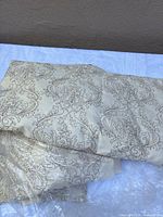Folded beige embroidered curtain panels showing scroll motif