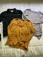 Three tops laid out: plaid shirt, mustard yellow top, grey dotted top