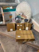 Group shot showing all items on stairs: NutriBullet Baby box, nursing pillow package, grey bra, three gold boxes of swaddles, sealed hanger carton